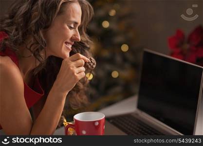 Happy woman having christmas cookies with cup of hot chocolate and usign laptop
