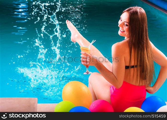 Happy woman having fun with balloons and cocktail drink alcohol splashing water. Pretty attractive girl relaxing at swimming pool edge poolside.. Happy woman with balloons and cocktail at poolside