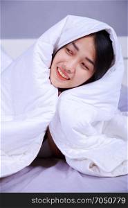 happy woman hiding under blanket on bed in the bedroom