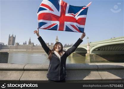 Happy woman holding British flag while standing against Big Ben at London; England; UK
