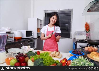 happy woman holding purple cabbage and knife in kitchen room at home