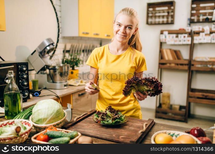 Happy woman holding salad on the kitchen, cooking healthy bio food. Vegetarian diet, fresh vegetables and fruits on wooden table