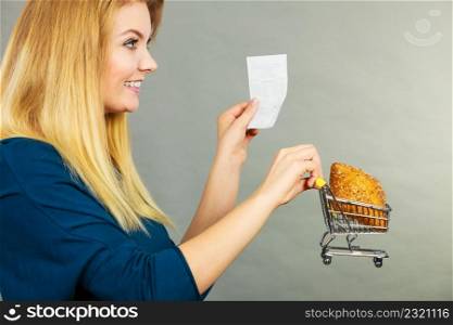 Happy woman holding shopping basket with bread looking at bill receipt, enjoying low prices.. Happy woman holding shopping basket with bread