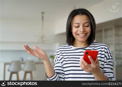 Happy woman holding smartphone, looking at mobile phone screen, reading good news in message, standing at home. Astonished smiling female using mobile app, received cashback, online store discount.. Female holding phone, reading good news message, happy with cashback, online store discount at home