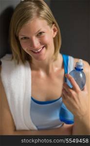 Happy woman holding water bottle in locker room at gym