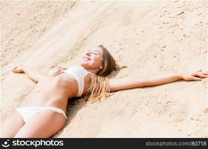 happy woman in a white bikini resting on the sand