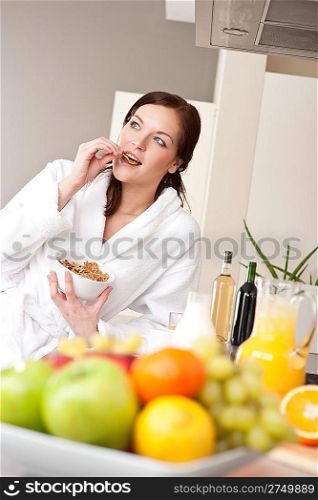 Happy woman in bathrobe eat cereals for breakfast in kitchen