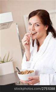 Happy woman in bathrobe eating healthy cereals for breakfast in kitchen