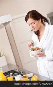 Happy woman in bathrobe eating healthy cereals for breakfast in kitchen