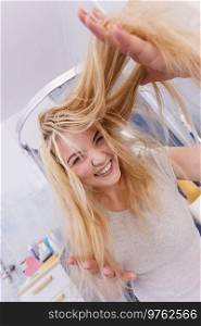 Happy woman in bathroom having wet long blonde hair. Playful young teenage female taking care of her hairdo.. Happy woman playing with wet hair