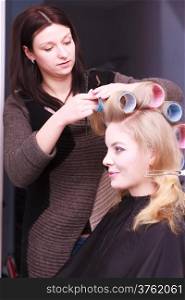 happy woman in beauty salon. Cheerful blond girl with hair curlers rollers by hairdresser. Hairstyle.