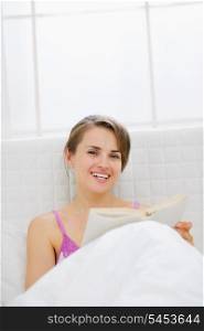 Happy woman in bed reading book
