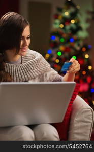 Happy woman in front of Christmas tree making online purchases