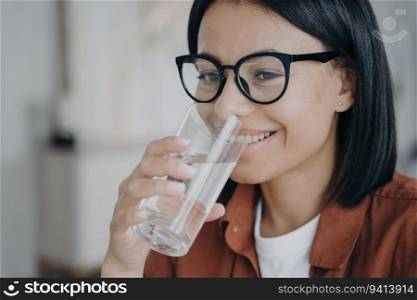 Happy woman in glasses drinks clean, filtered water from a glass. Prevents dehydration, maintains water balance, and promotes healthy skin.