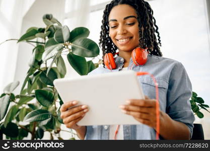 Happy woman in headphones choosing music on tablet pc. Pretty lady in earphones relax in the room, female sound lover resting. Woman in headphones choosing music on tablet pc