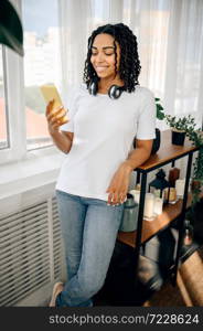 Happy woman in headphones listen to music from mobile phone. Pretty lady in earphones relax in the room, female sound lover resting. Woman in headphones listen to music from phone