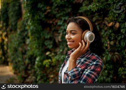 Happy woman in headphones listening to music in summer park. Female music fan walking outdoors, girl in earphones, outdoors. Woman in headphones listening to music in park