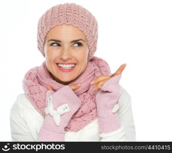 Happy woman in knit scarf, hat and mittens pointing on copy space