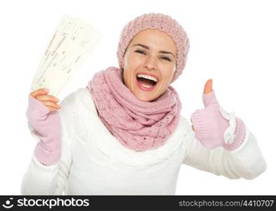 Happy woman in knit winter clothing holding air tickets and showing thumbs up