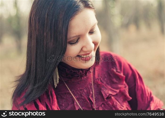 Happy woman in red dress smiling looking down in front of nature background