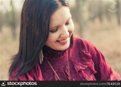 Happy woman in red dress smiling looking down in front of nature background