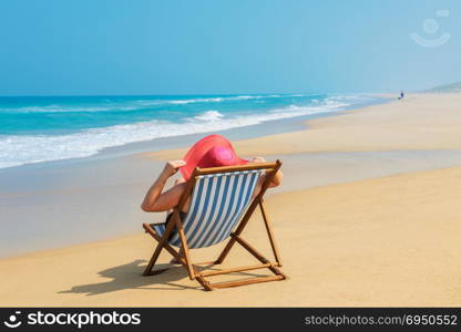 Happy woman in red sunhat on the beach sitting on deckchair and looking into the sea.Vacation and travel concept.