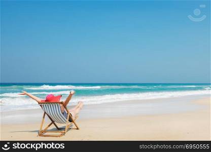 Happy woman in red sunhat on the beach sitting on deckchair with hands up.Vacation and travel concept