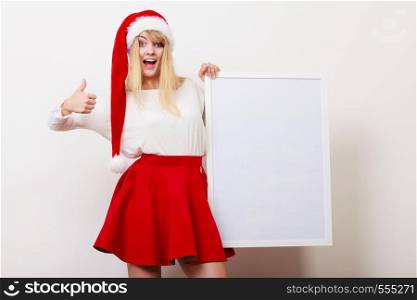 Happy woman in santa claus hat holding empty blank banner with copy space. Pretty girl in studio on gray. Christmas xmas advertisement.