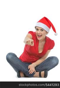 Happy woman in Santa hat sitting on floor and pointing in camera
