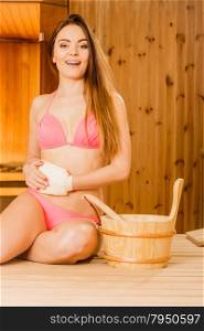 Happy woman in sauna with exfoliating glove.. Happy young woman in wood finnish spa sauna massaging skin with exfoliating glove. Girl in bikini relaxing. Skincare concept.