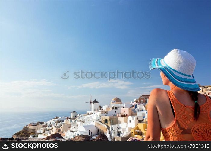 Happy woman in sun hat enjoying her holidays on Santorini island, Greece. View on Caldera and Aegean sea from Oia. Travel, tourist concepts