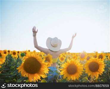 Happy woman in sunflower field. Summer girl in flower field cheerful and joyful.Caucasian young lady in cowboy hat dancing, smiling elated and serene with arms raised up.. Happy woman in sunflower field