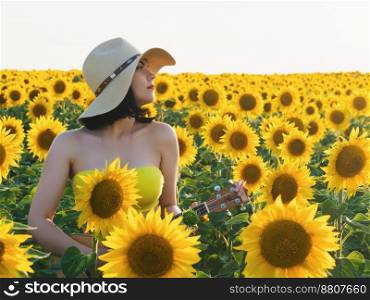 Happy woman in sunflower field. Summer girl in flower field cheerful and joyful.Caucasian young lady in cowboy hat dancing, smiling elated and serene with arms raised up.. Happy woman in sunflower field playing on ukulele