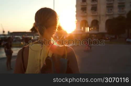 Happy woman in sunglasses walking outdoor with shopping bags on the shoulder. She turning, smiling and walking away