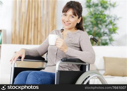 happy woman in wheelchair holding a hot drink at home