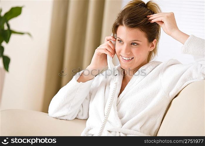 Happy woman in white bathrobe with phone home calling in lounge