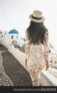 Happy woman in white dress and straw hat enjoying her holidays on Santorini island. Europe summer travel destination. Greek Islands