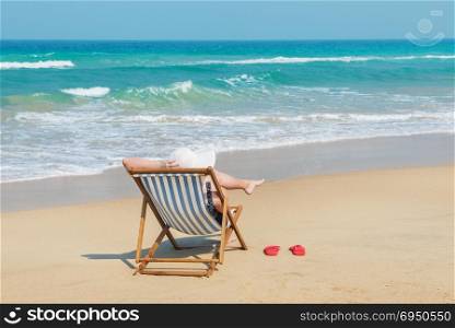Happy woman in white sunhat on the beach sitting on deckchair .Vacation and travel concept.