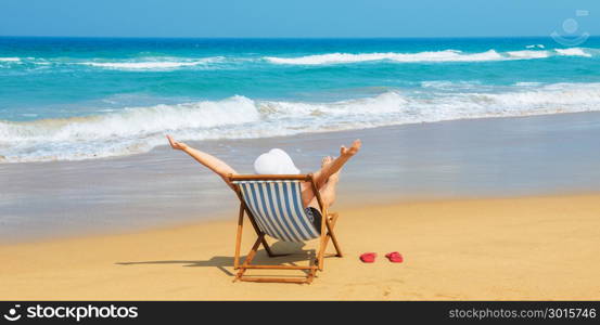 Happy woman in white sunhat on the morning beach sitting on deckchair with hands up.Vacation and travel concept.