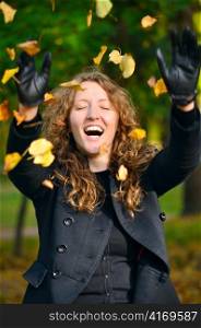 happy woman is throwing dry autumn leaves in park