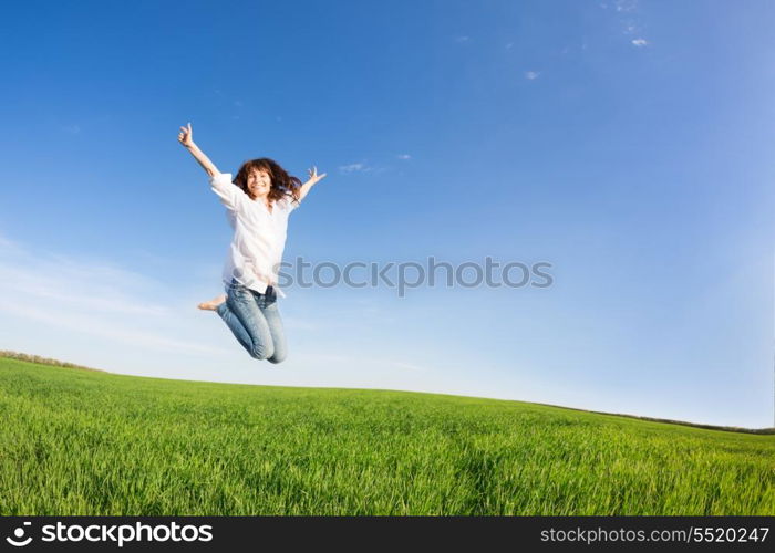 Happy woman jumping in green field against blue sky. Summer vacation concept