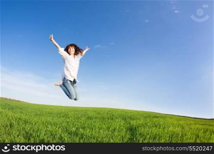 Happy woman jumping in green field against blue sky. Summer vacation concept
