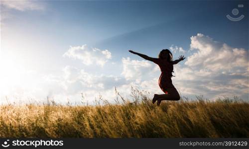 Happy woman jumping in the meadow at the sunset