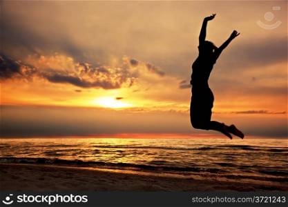 Happy woman jumping on the beach at sunset. Success, energy, wellbeing concepts