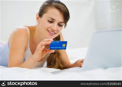Happy woman laying on bed with laptop and shopping on net