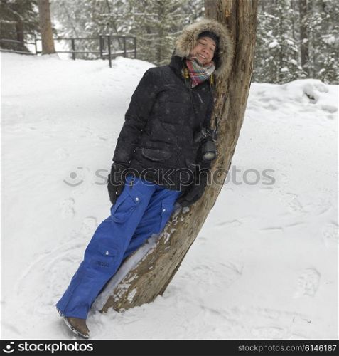 Happy woman leaning on a tree in snow covered forest, Johnston Canyon, Banff National Park, Alberta, Canada