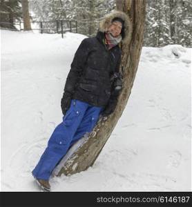 Happy woman leaning on a tree in snow covered forest, Johnston Canyon, Banff National Park, Alberta, Canada