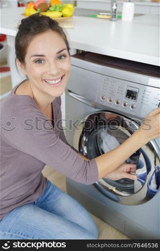 happy woman loading dirty clothes in washing machine