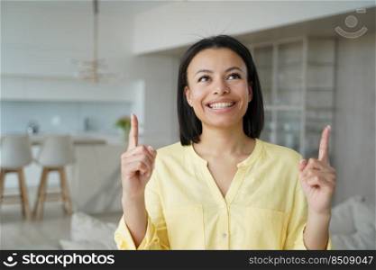 Happy woman look up pointing up with fingers. Smiling excited female client customer showing special online store offer, holding finger up, demonstrating new product, amazing news, standing at home.. Happy female customer pointing up with fingers, showing online store offer, amazing news at home
