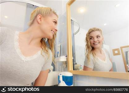 Happy woman looking at herself in mirror having wet blonde hair. Positive clean female.. Woman with wet blonde hair